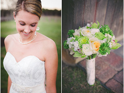 A bride in a strapless white wedding dress smiling and looking downward. She wears a pearl necklace and earrings. To the right, a bouquet featuring white, green, and yellow flowers is propped against a wooden wall on the ground.