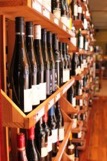 A store display with wooden shelves filled with numerous wine bottles. The shelves are well-organized, with wine bottles aligned in rows. The background is slightly out of focus, showcasing more wine bottles and the warm interior of the store.