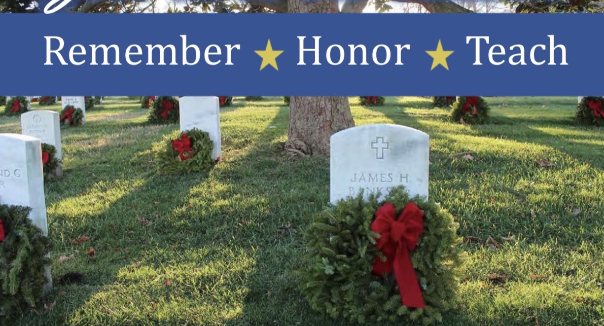 A cemetery with rows of tombstones, each adorned with a holiday wreath featuring a red bow. A banner above reads, "Remember ★ Honor ★ Teach." In the background, there are more gravestones and large trees casting shadows on the grass.