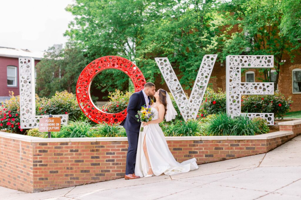 A bride and groom kiss in front of a large, decorative 