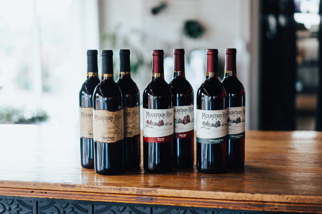 Five bottles of wine with various labels are displayed on a wooden table indoors.