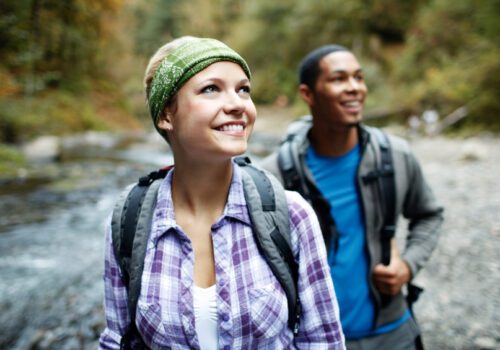 two hikers smiling and walking along a river