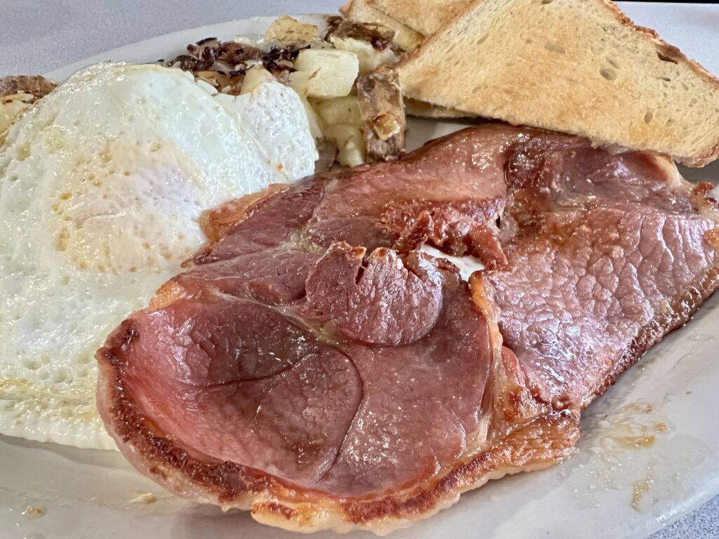 slice of country ham, eggs, and toast on a plate