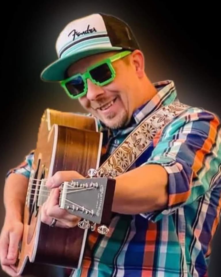 male with green glasses smiling and holding a guitar