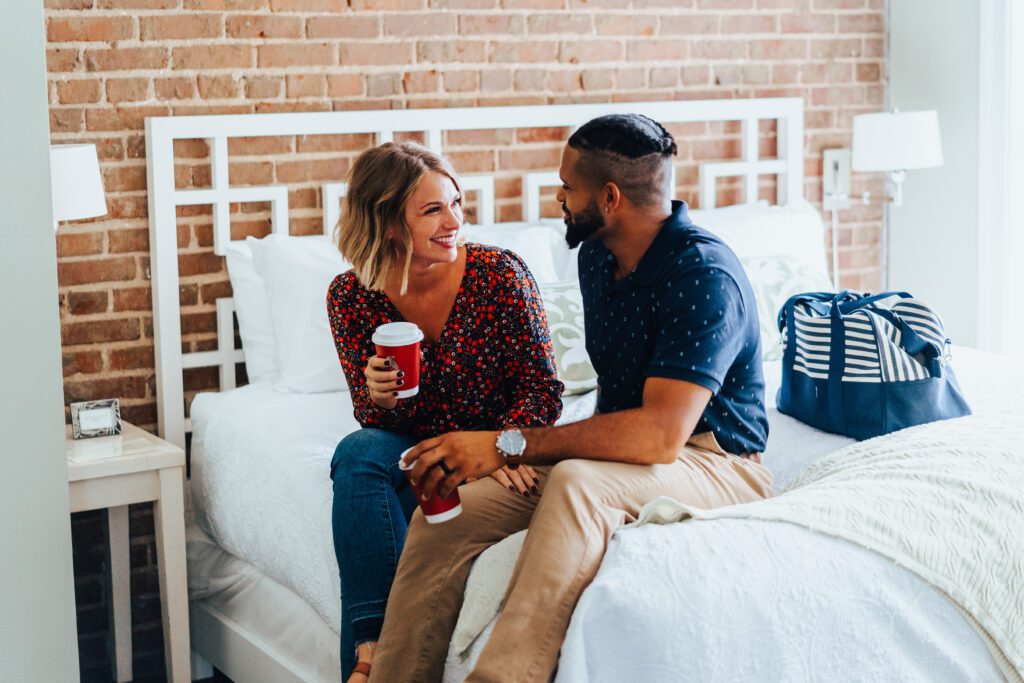 male and female sitting on bed drinking coffee