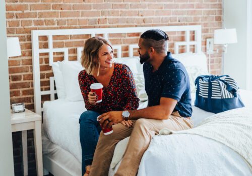 male and female sitting on bed drinking coffee