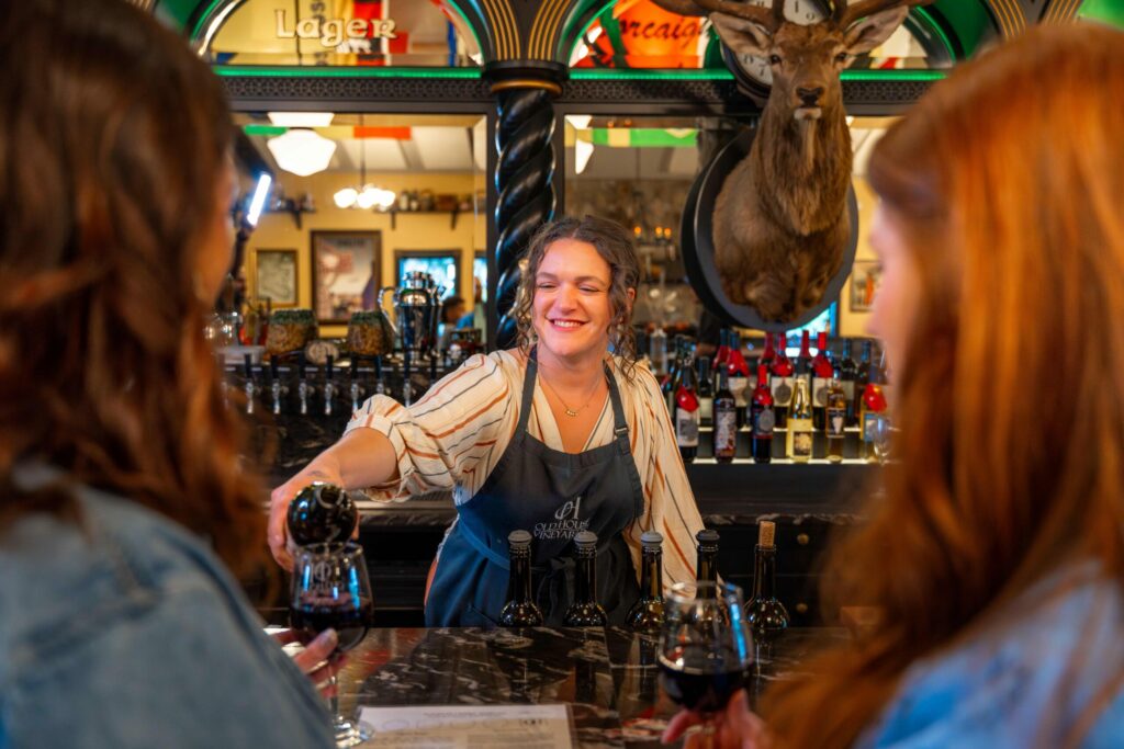 two women standing at a bar with a female bartender pouring wine