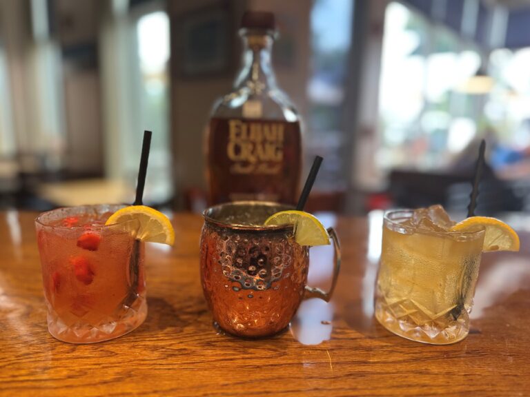 a bottle of Elijah Craig and three mixed drinks in front