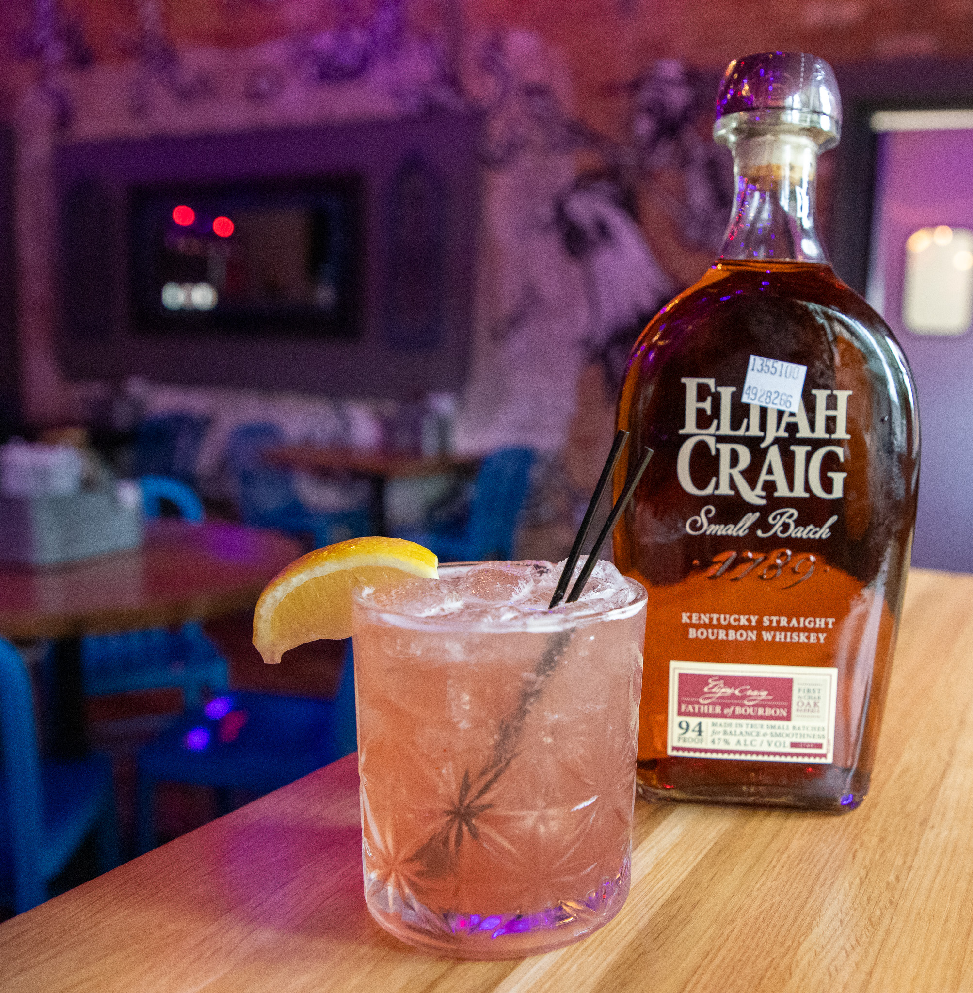 bottle of Elijah Craig and a pink drink with ice and a lemon