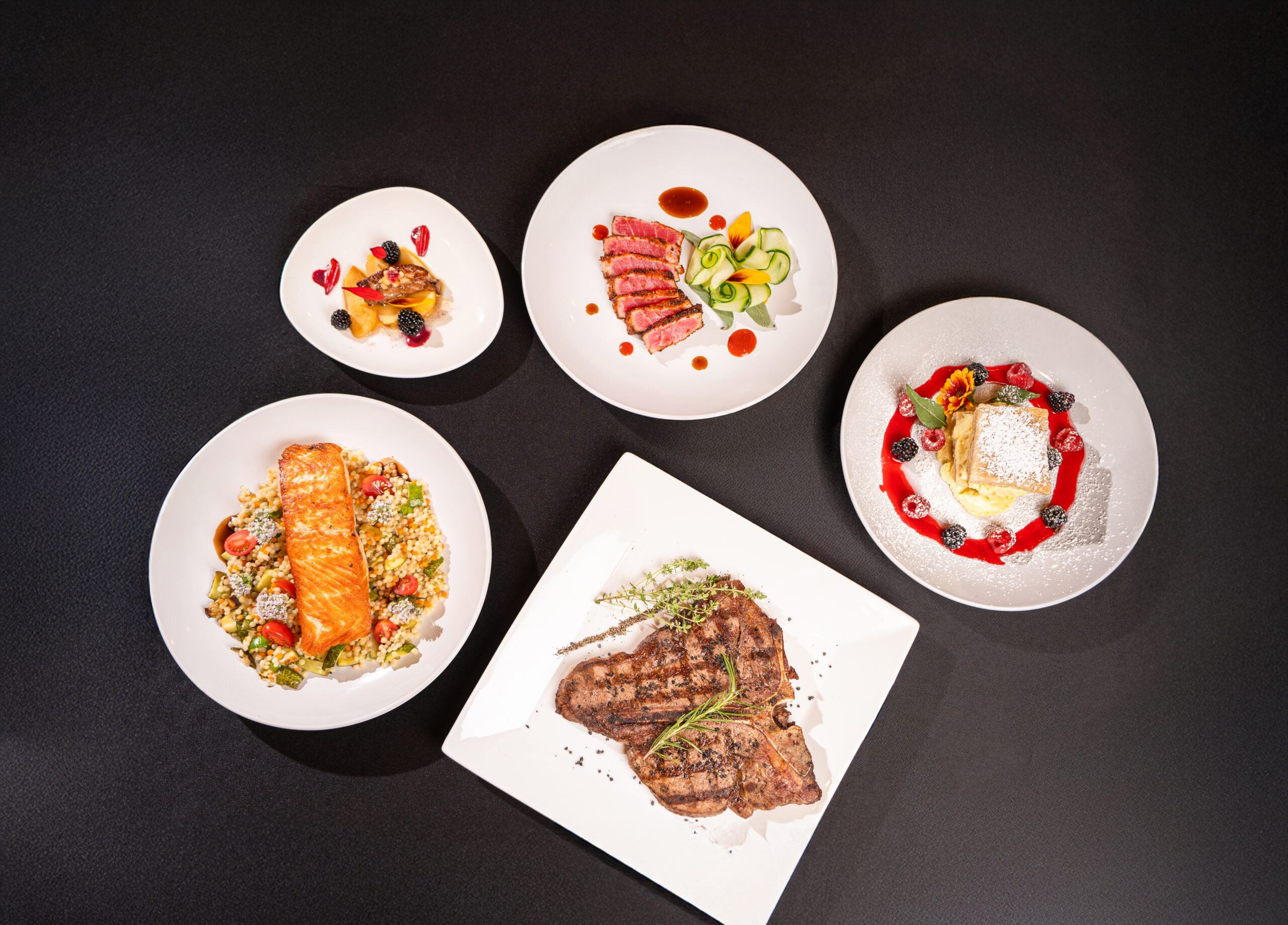 5 dishes laid out with plated food on a black tablecloth