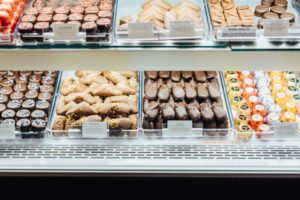 A display case filled with an assortment of chocolate confections, including dark chocolate pieces with sprinkles, milk chocolate squares, and chocolate-covered nuts. Small labels can be seen in front of each type of candy.